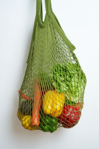 A vertical shot of an eco-friendly mesh bag with various vegetables on a white background