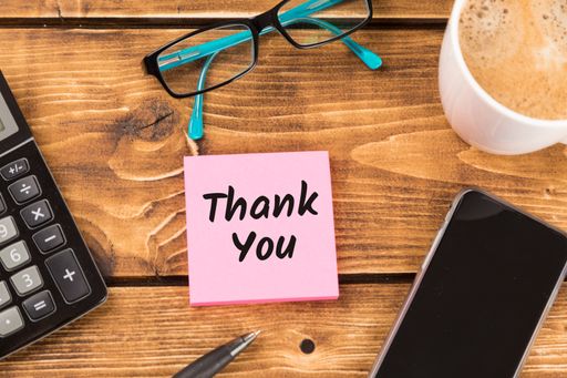 A top view of a "Thank you" text on sticky note on a desk with a calculator, phone, and a cup of coffee on it