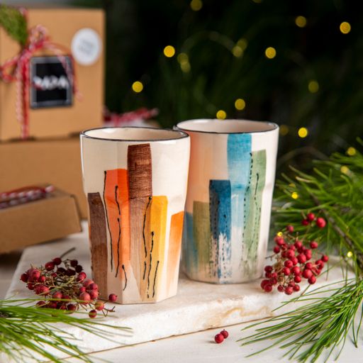 A closeup of colorful mugs on the table with Christmas decorations on it