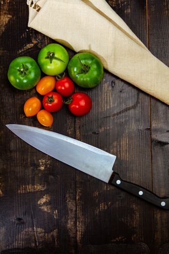 A high angle shot of ripe and unripe tomatoes with knife and napkin on a wooden table