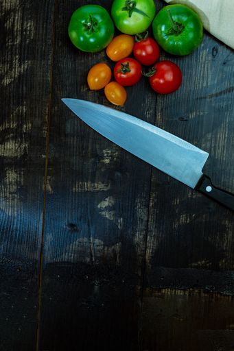 A vertical top view of ripe and unripe tomatoes with a knife on a wooden table