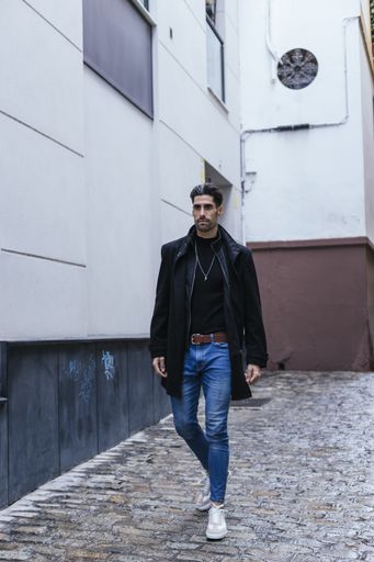 A vertical shot of a serious young man wearing a black coat walking outside