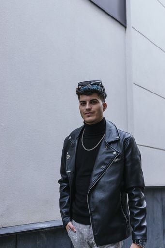 A young stylish man with colorful hair wearing a turtleneck, leather jacket, sunglasses, necklace