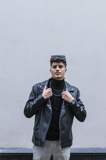 A young stylish man with colorful hair wearing a turtleneck, leather jacket, sunglasses, necklace