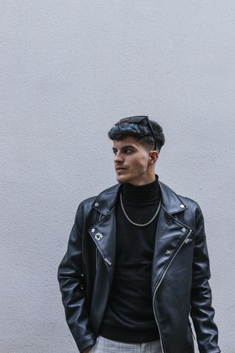 A young stylish man with colorful hair wearing a turtleneck, leather jacket, sunglasses, necklace