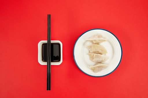 A top view closeup of cooked dumplings on a white plate next to a soy sauce on a red background