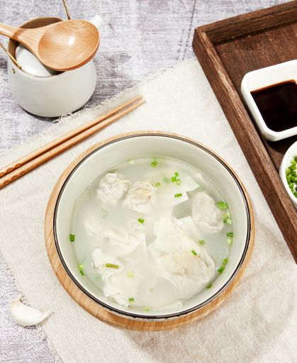 A top view closeup of a dumpling soup, soy sauce, chopsticks and chopped green onion