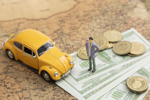 A top view closeup of a toy car, with coins and banknotes and a man figure toy on a map