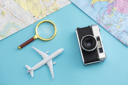 A top view of a camera, airplane toy and magnifying glass on a blue background with a map