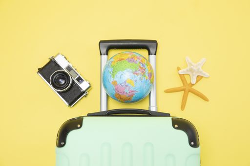 A top view of a suitcase, globe, camera and starfishes on a yellow background - vacation concept