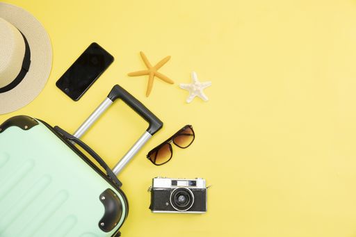 A top view of a suitcase, hat, phone, camera and starfishes on a yellow background - vacation concept