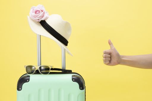 A closeup of a hand, sunglasses, hat, and luggage on a yellow background-concept travel