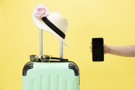 A top view of a suitcase, sunglasses, phone and hat on a yellow background - vacation concept