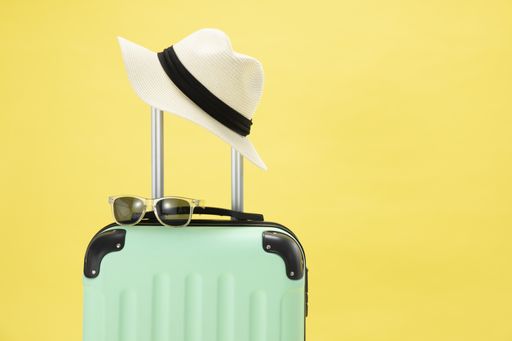 A top view of a suitcase, sunglasses, camera and hat on a yellow background - vacation concept