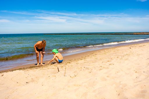 Two young boys standing on wet sand close by the water at a beach on a warm spring day.