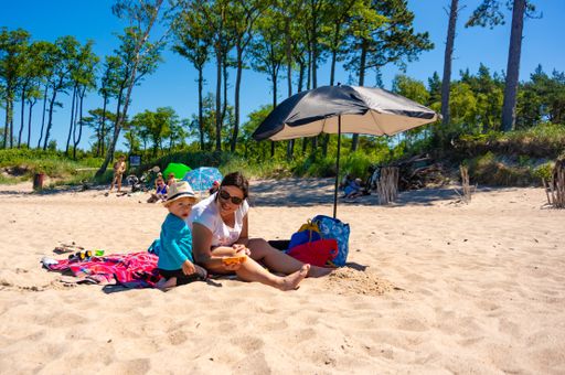 Woman and child sitting on a blanket under a umbrella on sand at a beach