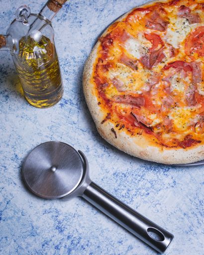 A top view of a pepperoni pizza, olive oil and a roller blade on a marble table