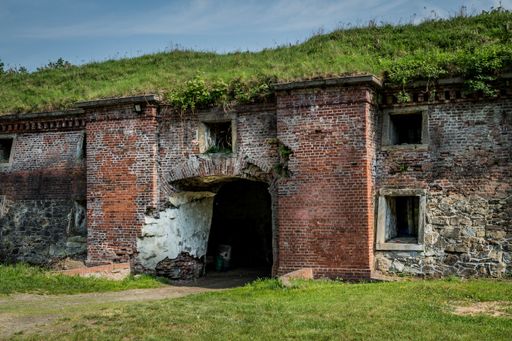 A stone building ruins in a garden covered in greenery under the sunlight