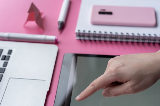 A high angle shot of a tablet, a cellphone, and writing tools on a pink surface