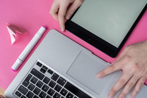 A high angle shot of a person working with a laptop and a tablet on a pink surface