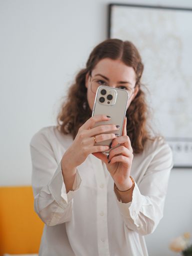 A vertical shot of a woman in a white shirt taking a photo with her smartphone