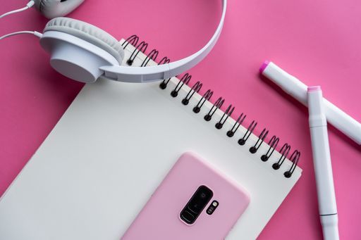 A top view of smartphone, markers, notebook, and headphones on pink background