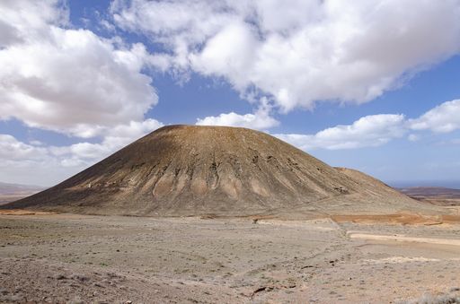 A hill in a field under a blue cloudy sky and sunlight at daytime