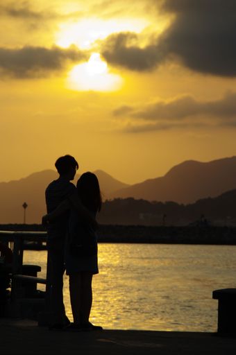 Vertical shot of the silhouette of a hugging couple by a lake, the mountains on the horizon, at the sunset