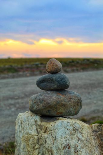 A pile of carefully balanced stones illuminated by a vibrant orange sunset sky in the blurred background