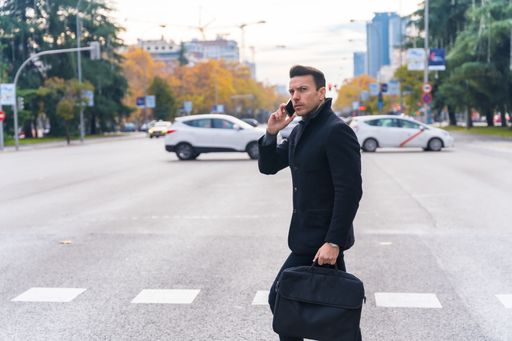 A middle-aged Caucasian businessman talking on the phone while crossing the road in the city