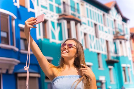 A portrait of a Caucasian blonde tourist with sunglasses, taking a selfie against colorful houses
