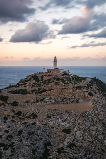 A vertical shot of a lighthouse on the rocky cliff captured in Mallorca, Spain