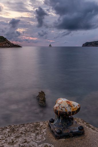 A vertical shot of the rusted pier on the calm and endless ocean captured in San Telmo, Mallorca