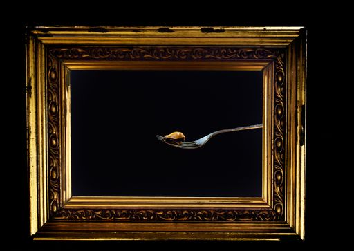 A vintage golden photo frame with single blue mussel on a fork against a black background