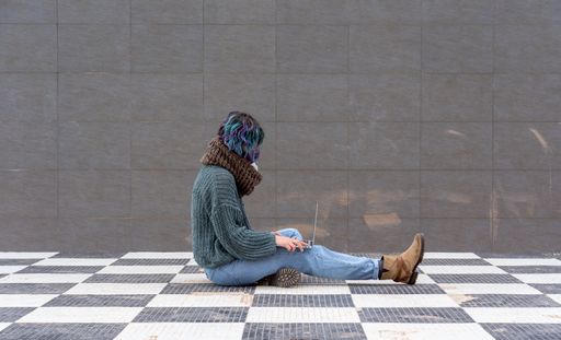 A closeup shot of a female in a facial mask sitting on a chess floor with a laptop - new normal concept