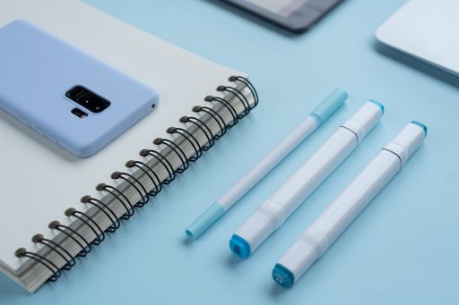 A close up shot of markers, pens, a notebook and a phone on a blue desk