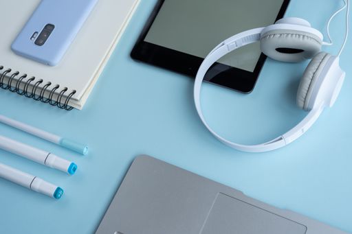 A high-angle shot of a laptop, markers, notebook, mobile phone, tablet and headphones on a blue desk