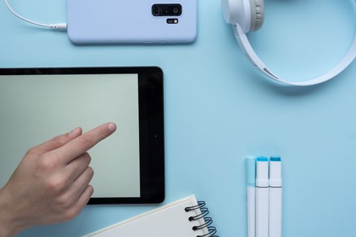 A high-angle shot of a person taking notes with a mobile phone, headphones, and markers