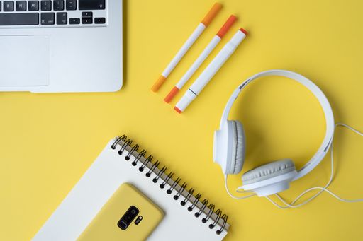 A high-angle shot of a laptop, markers, notebook, mobile phone and headphones on a yellow desk