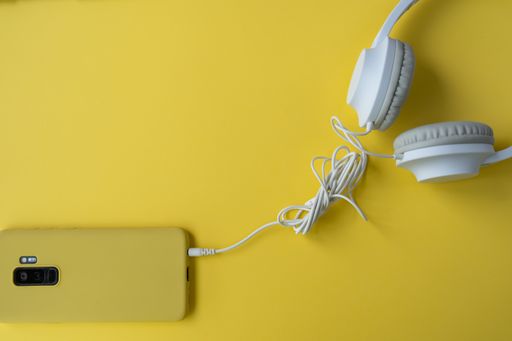 A top view of a phone with a yellow case and headphones on a yellow surface with a copy space