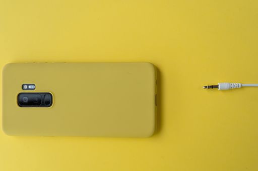 A top view of a phone with a headphone wire on a yellow surface
