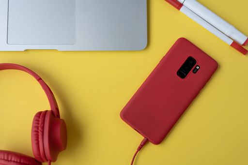 A top view of a red phone and headphones, a laptop on a yellow surface