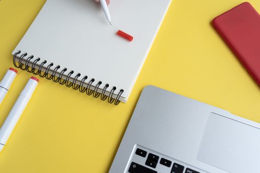 A closeup shot of a student working on a desk with a laptop and a notepad