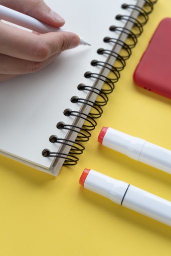 A vertical closeup shot of a person writing in a notepad
