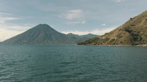 A landscape of the Lake Atitlan surrounded by hills under a blue sky in Guatemala