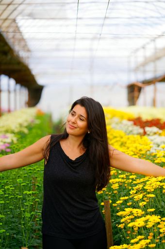 A vertical shot of a pretty Hispanic girl in a flower nursery against blurred background