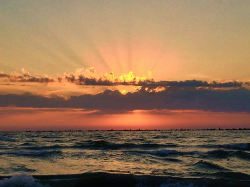 A shot of scenic sunrise over the wavy sea, the bright sun hidden behind the clouds