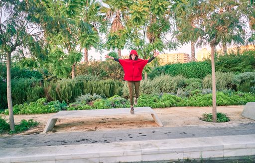 A young caucasian female with a red jacket jumping in a park