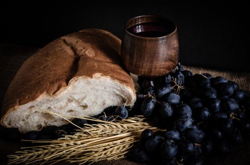 A closeup shot of wheat, white bread, grapes, and red wine in a wooden glass