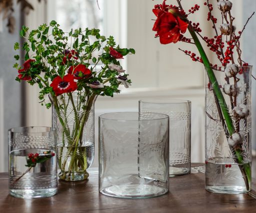 A selective focus shot of flowers in glass vases fwith water and empty glass vases on the table